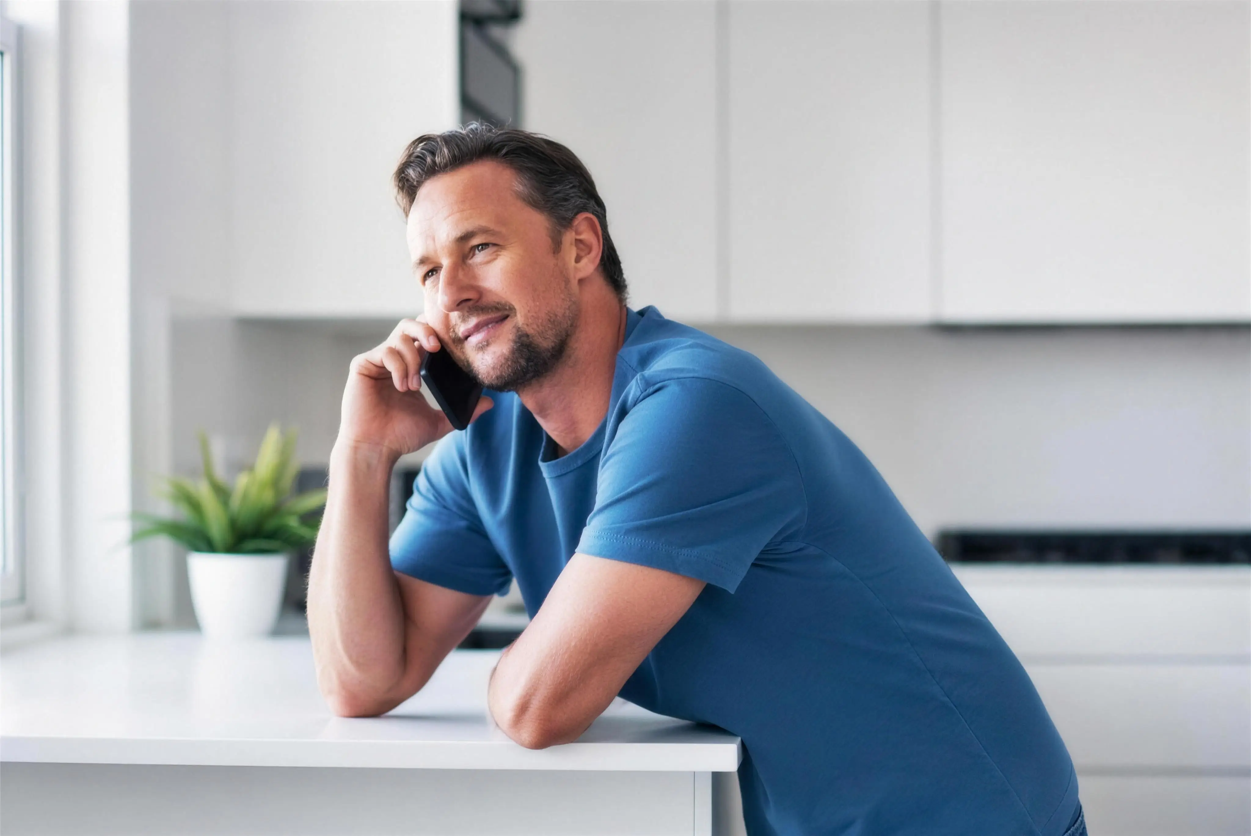 A man calmly making a phone call, leaning on his kitchen counter