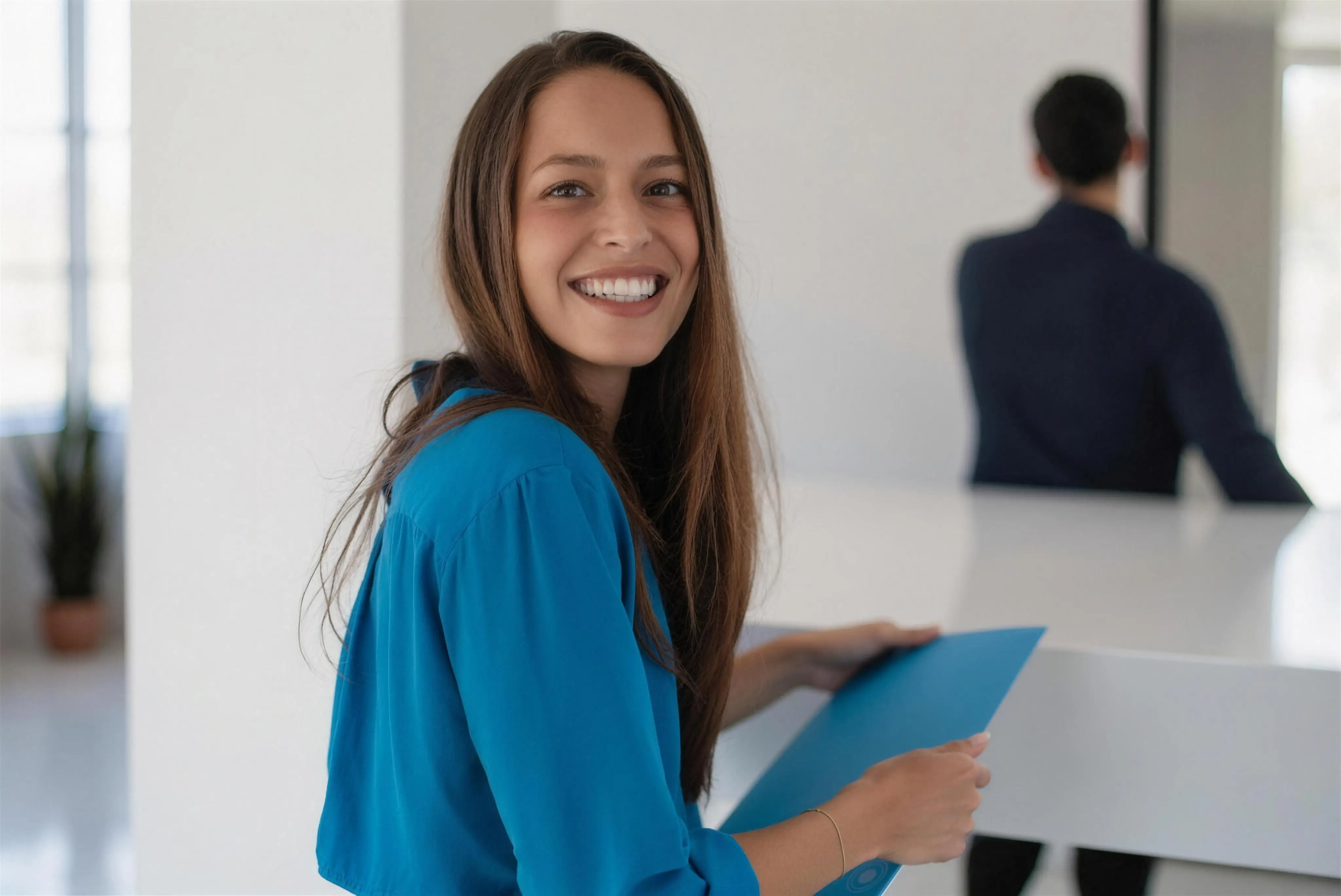 A new patient smiling at the front desk, holding her paperwork folder