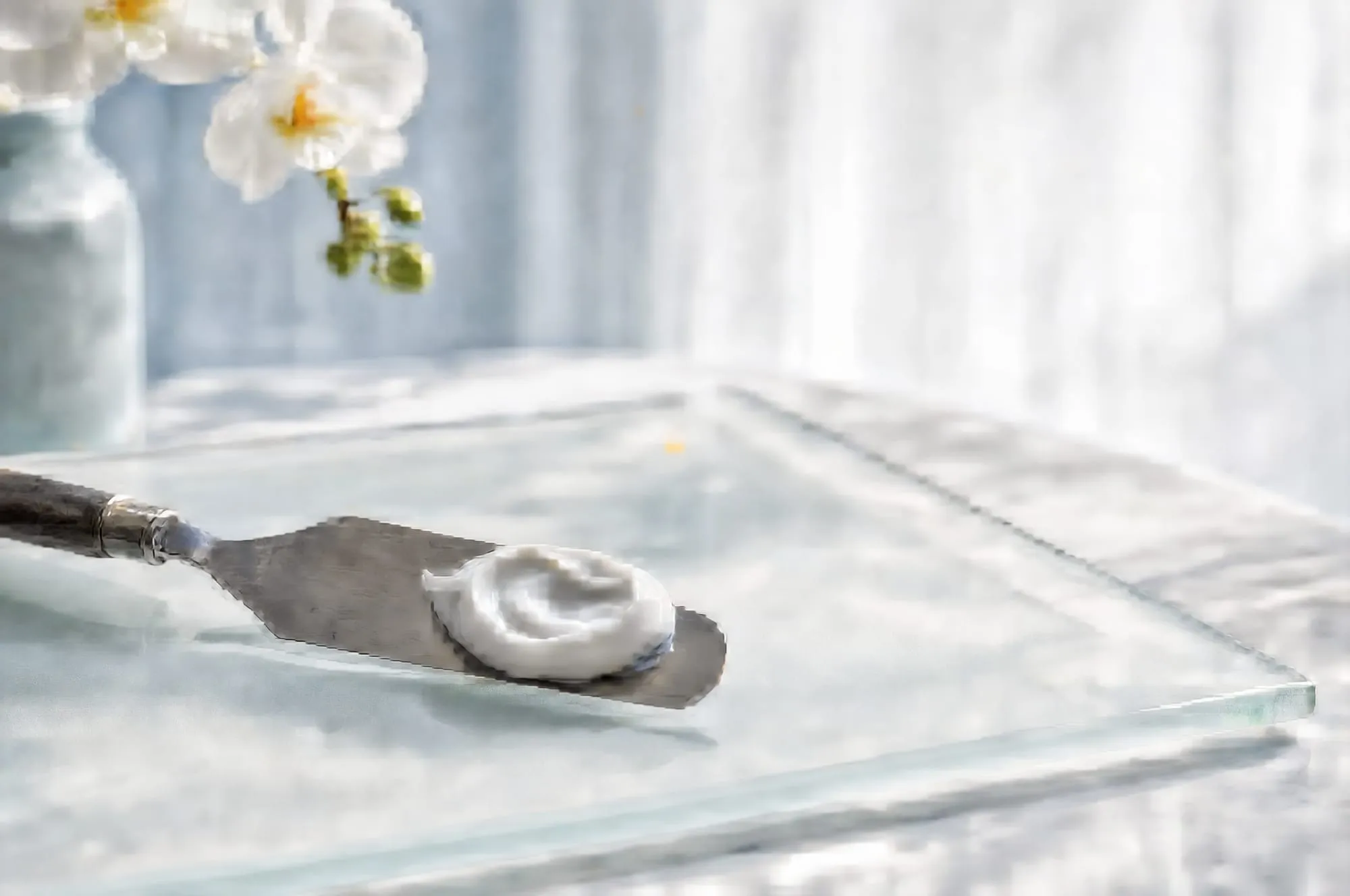 An artist palette knife holding white porcelain-tone paste on frosted glass