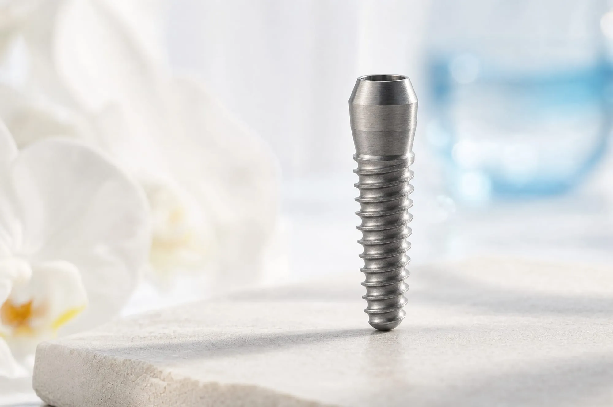 A brushed titanium implant post standing on white stone in soft morning light