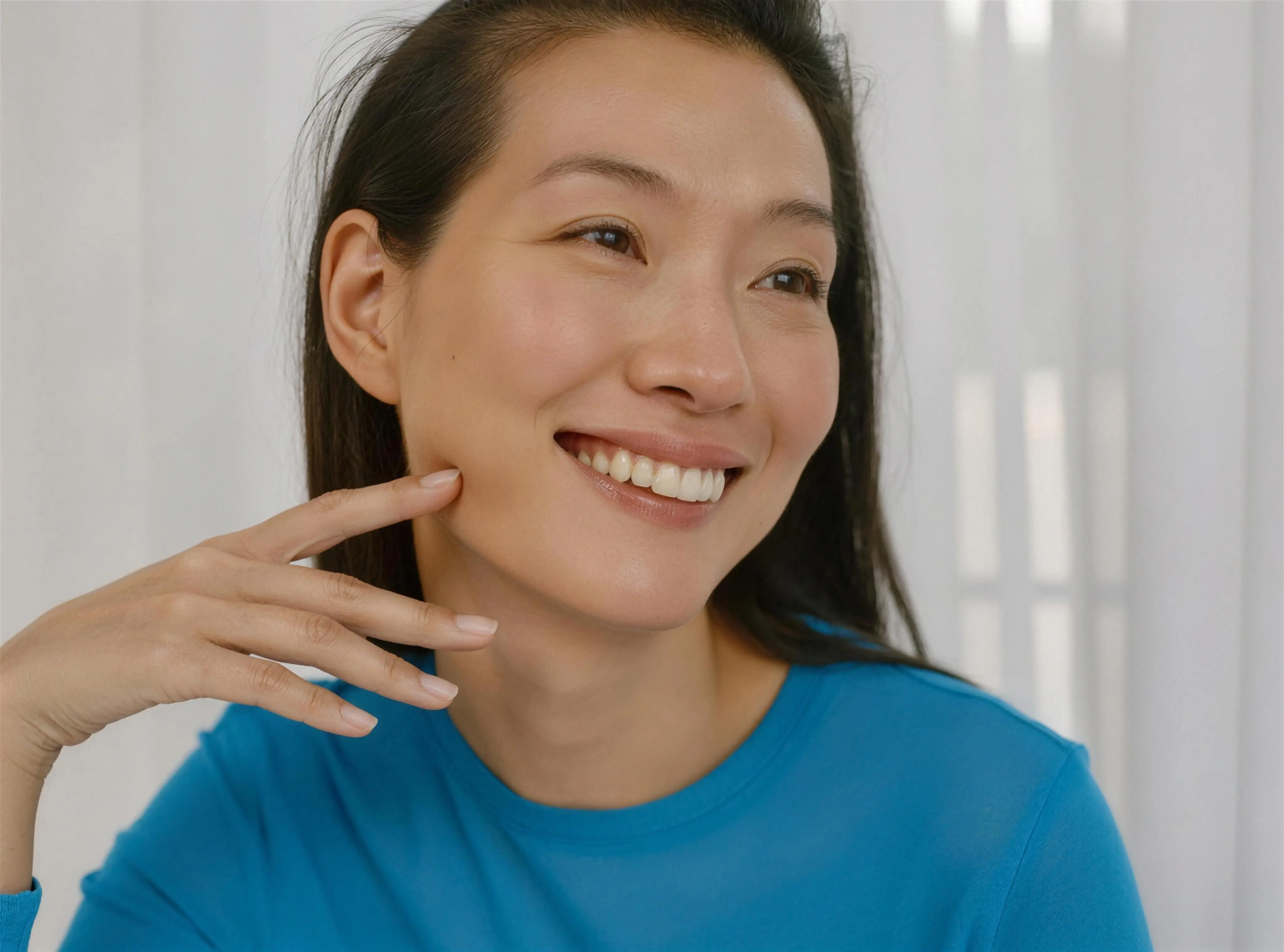 A woman smiling and touching her jawline in soft window light