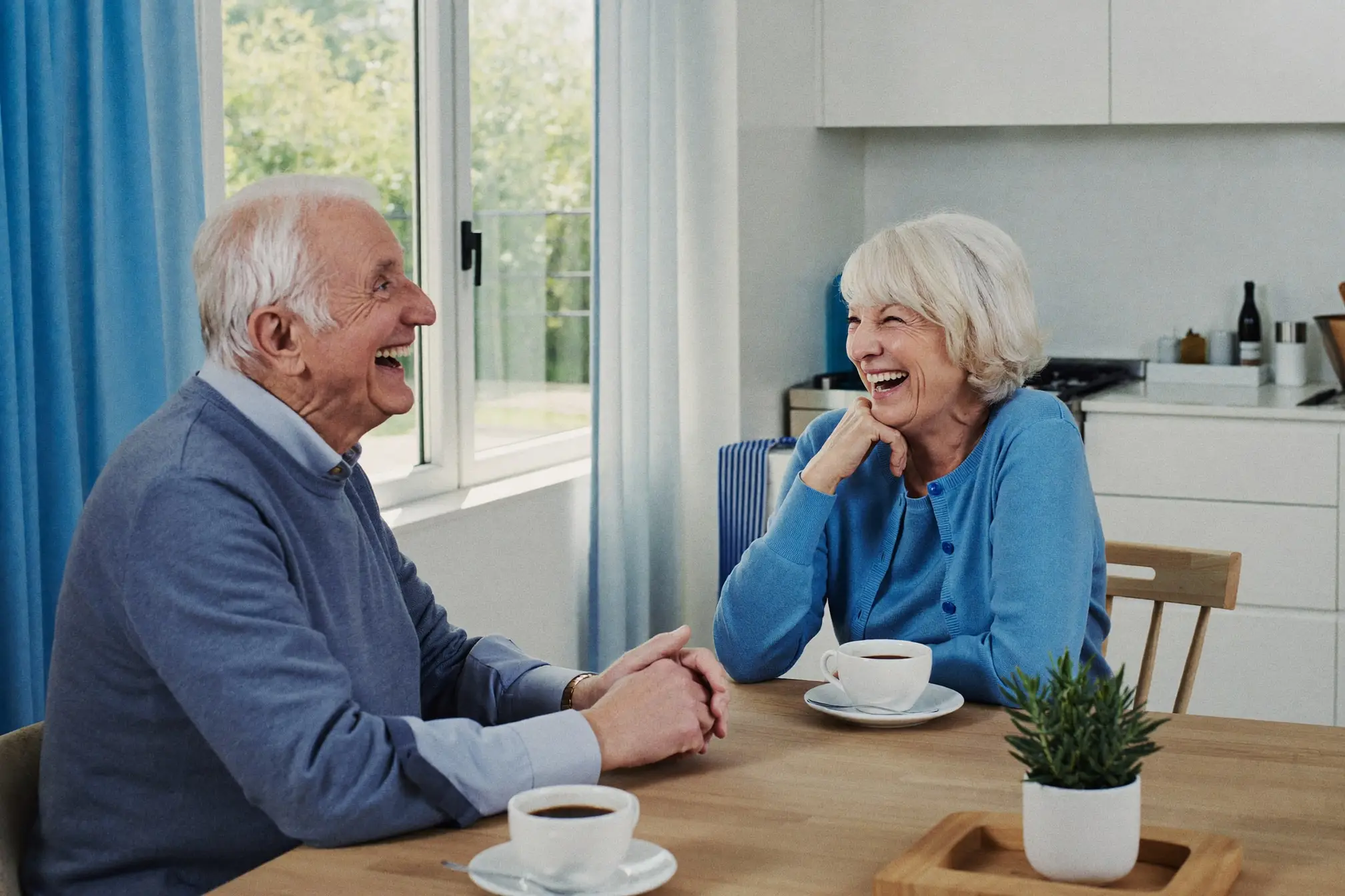 An older couple laughing together over coffee at their kitchen table