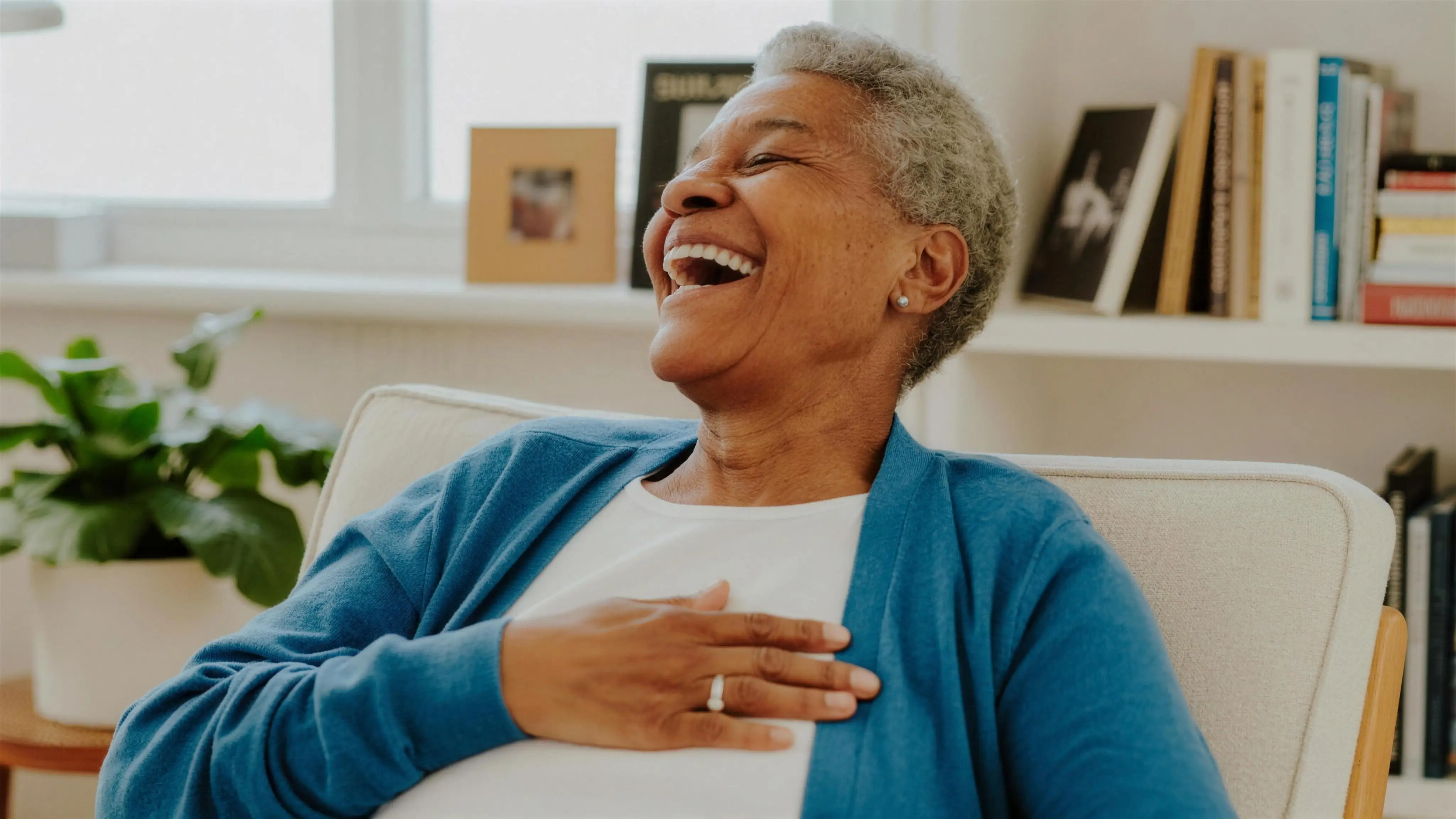 An older woman laughing joyfully in her armchair at home
