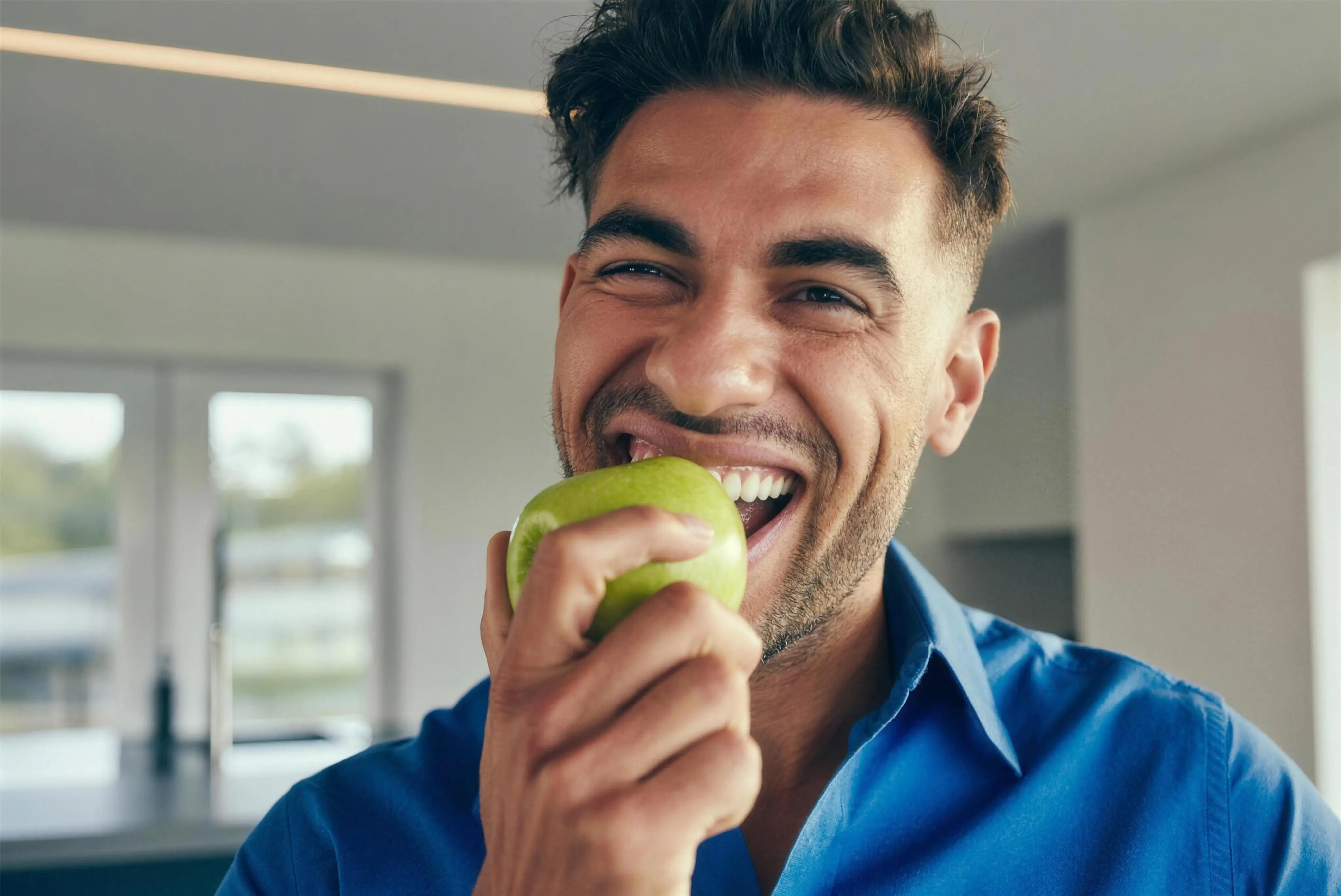 A man laughing as he bites into a crisp green apple