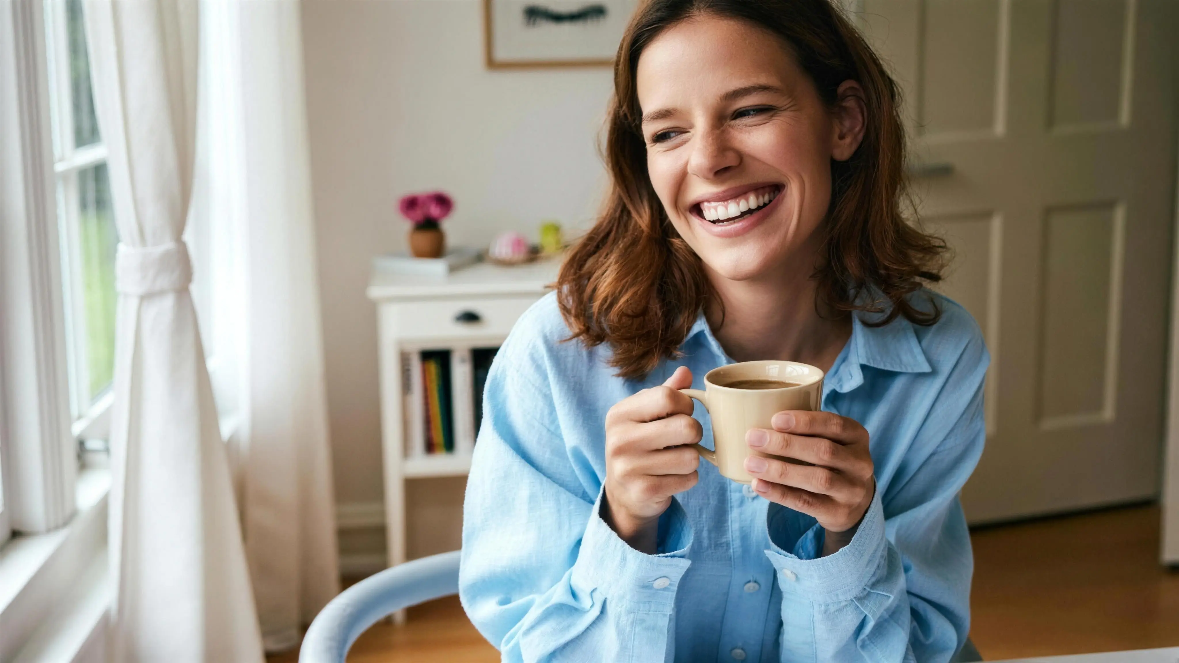A woman smiling over a warm mug of tea beside a bright window