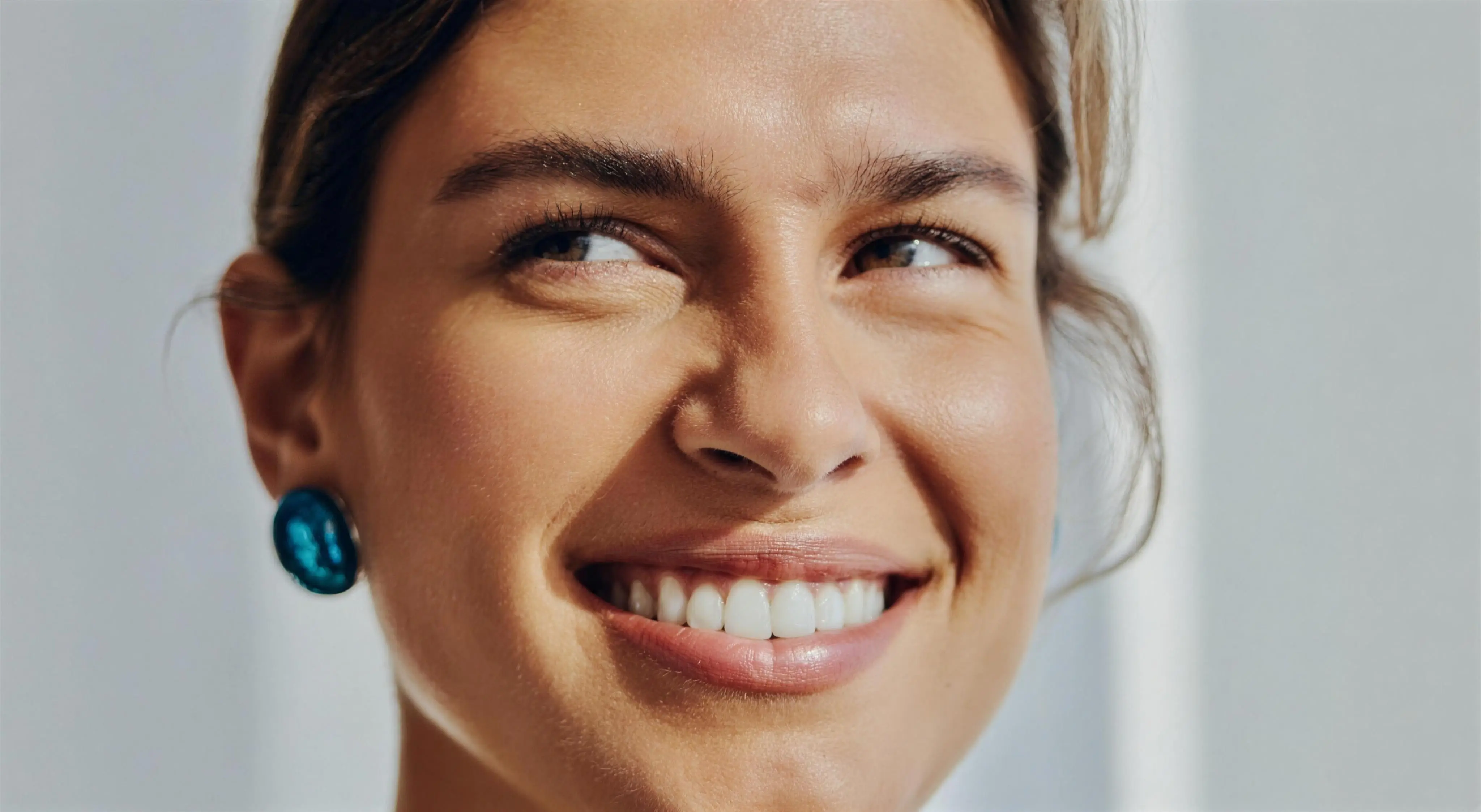 A close-up of a woman glancing aside with a bright, even smile