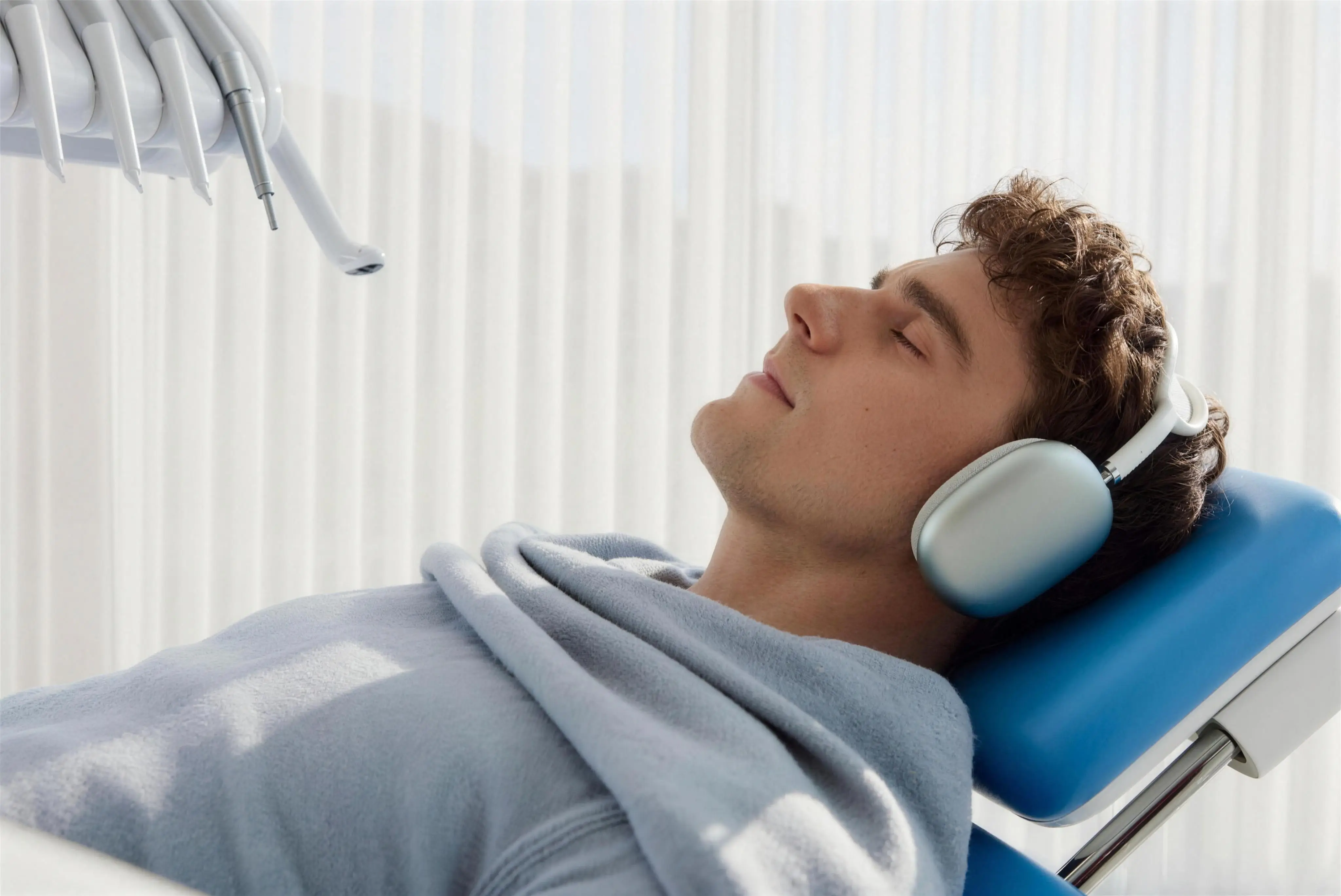A patient resting in the dental chair with headphones and a cozy blanket