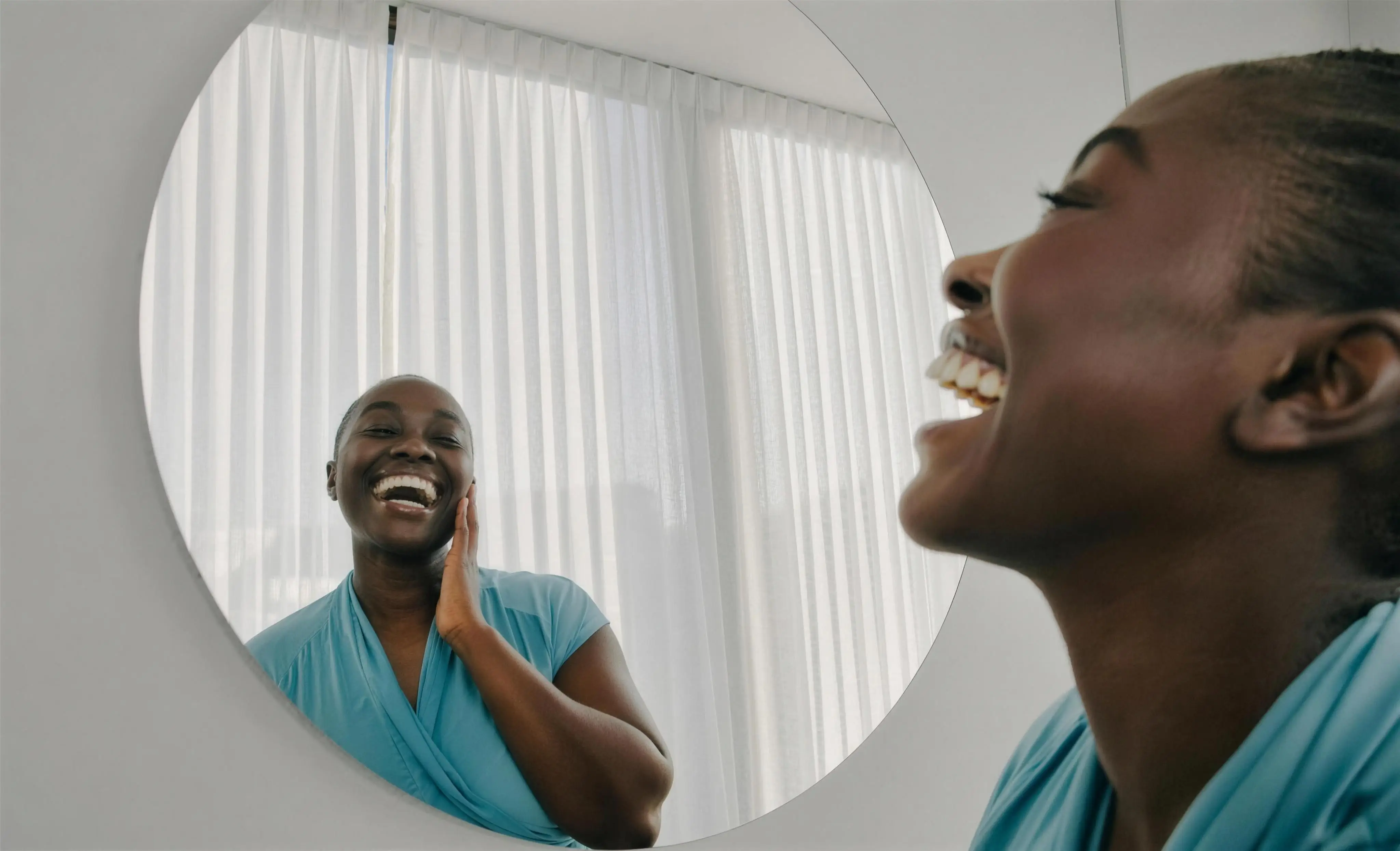 A woman laughing at her own reflection in a round mirror