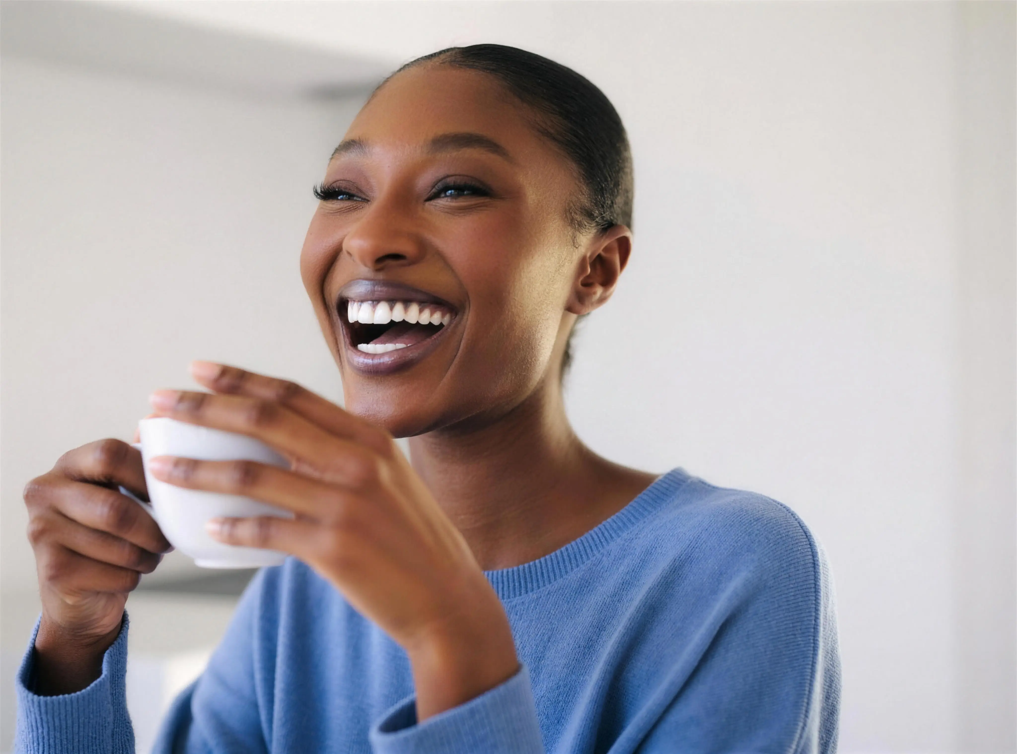 A woman with a bright smile laughing over a cup of coffee