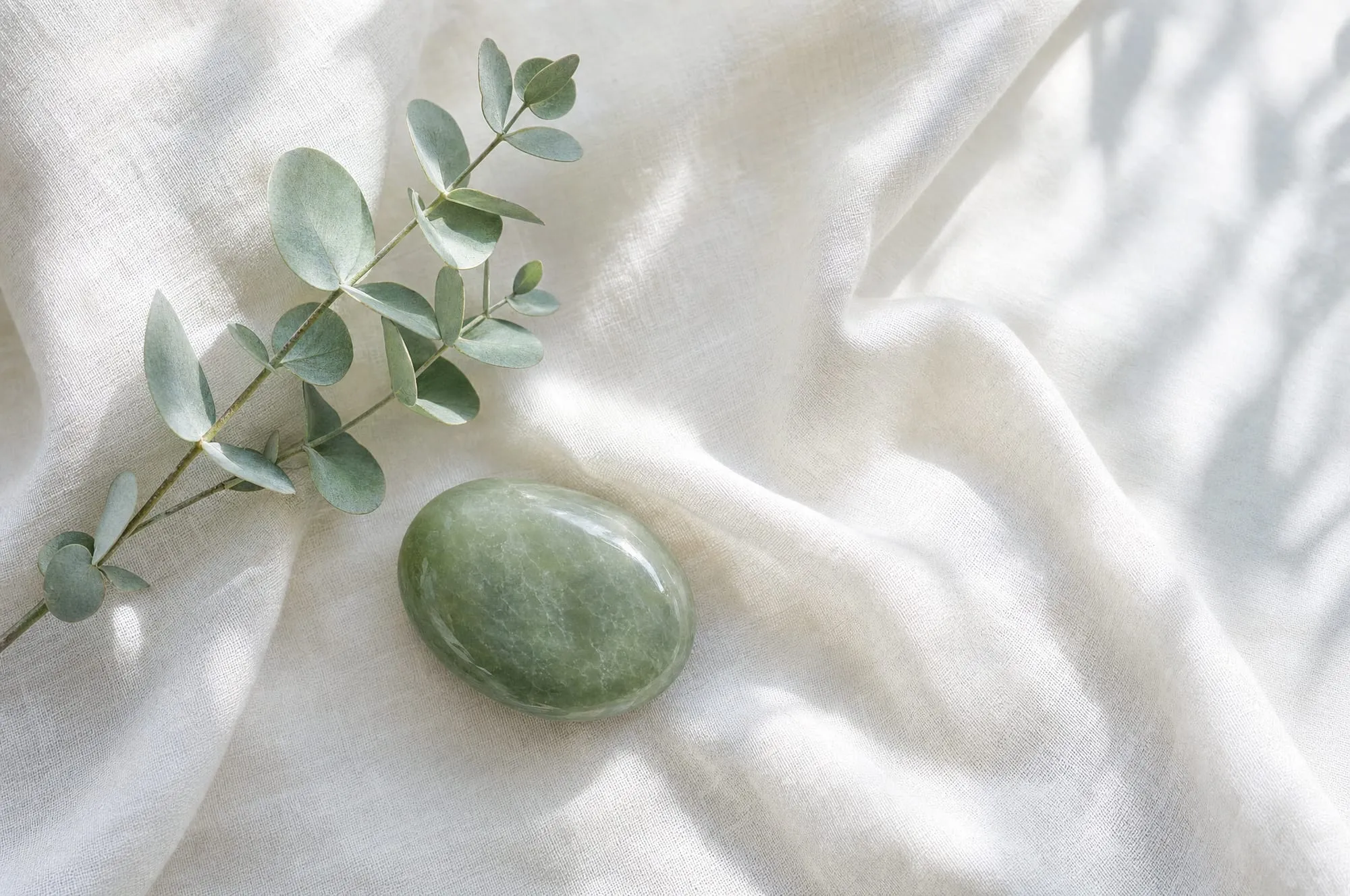 A eucalyptus sprig and smooth jade stone resting on ivory linen