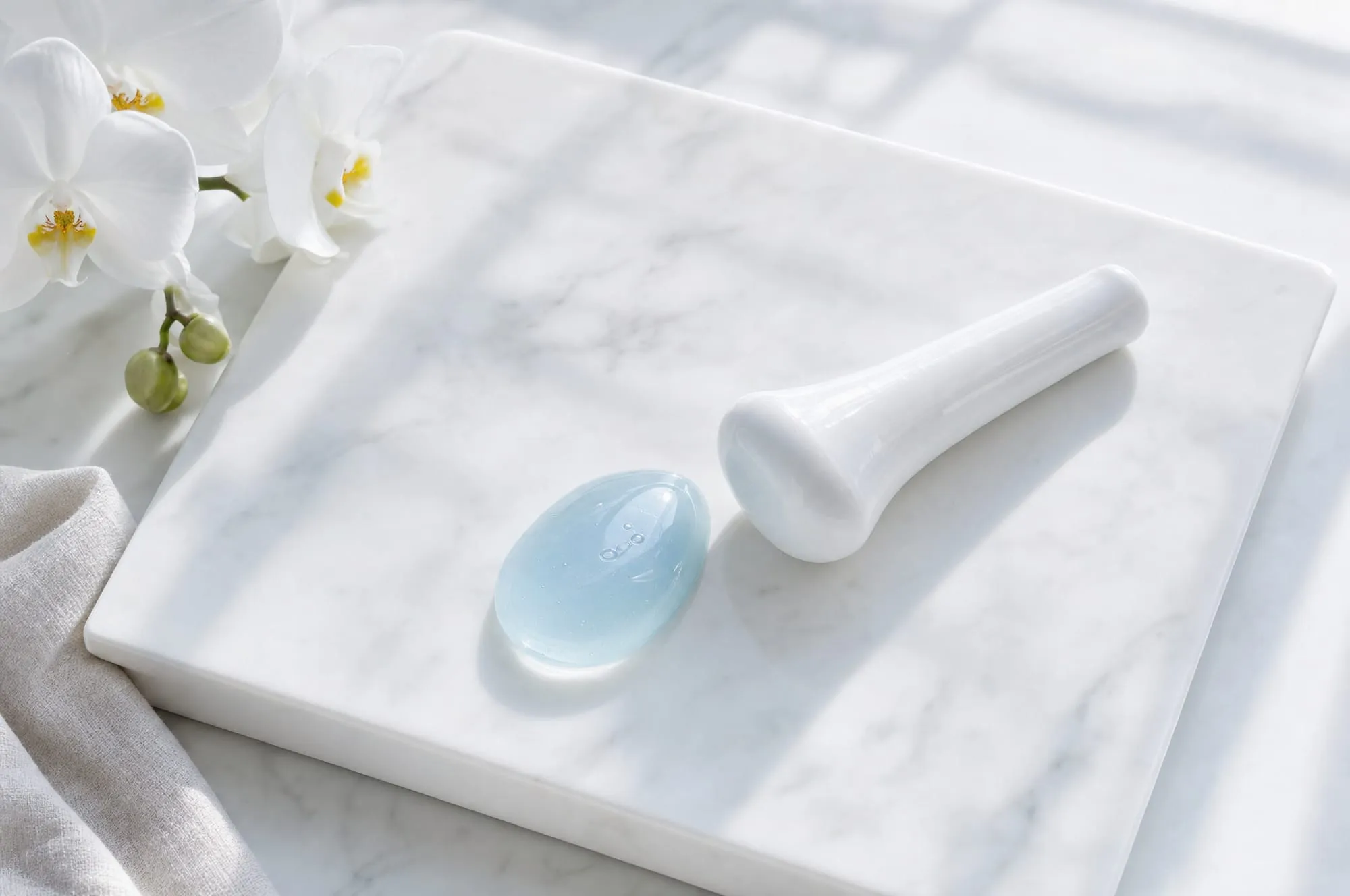 A white ceramic dish beside a swatch of pale blue whitening gel on porcelain tile